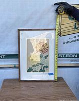 Framed wood block print showing flower artwork with tape measure held vertically showing height about 22.5 inches