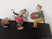 Three vintage wind-up tin toys: sailor playing accordion, bear in colorful outfit, and clown with cane