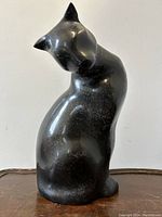 Front view of black patinated metal modernist cat sculpture showing smooth, stylized feline figure with head bowed.