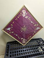 Top-down photo showing the full square framed embroidered floral panel with burgundy background and intricate detailed embroidery of bell flowers and poppies in corners and edges.