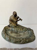 Front side view of antique Arabian snake charmer statue ashtray, showing figure kneeling and playing flute with detailed base.