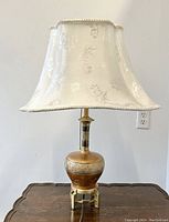 Full view of the vintage brass table lamp with white floral silk shade on wooden table.
