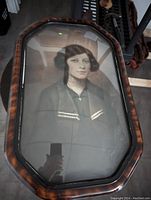 Full shot of the curved glass octagonal framed portrait painting showing the serene lady and wood frame on the floor.