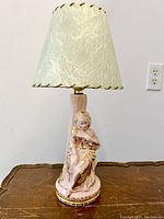 Front view of the pink ceramic lady lamp with parchment shade on a wooden surface.