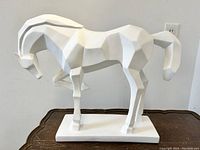 Front view of white cubist style equestrian horse sculpture on wooden table. Shows angular geometric facets and one leg raised.