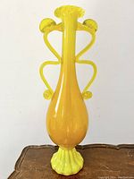 Front view of the tall electric yellow Murano glass amphora-shaped vase on a wooden surface.