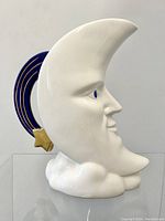 Side view of white ceramic crescent moon jug pitcher showing the man's face, the blue and gold crescent handle with a gold star, and the cloud base.