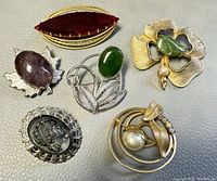 Six assorted vintage costume brooches on textured surface showing designs.