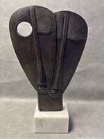 Full view of the sculpture showing abstract faces and the marble base.