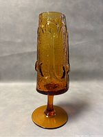 Front view of amber glass pedestal vase showing textured and sculptural details.