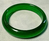 Close-up photo showing the top view of the solid green jade bangle on a textured surface.