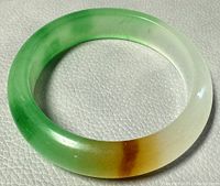 Close-up view of the jade bangle showing green, white, and brown gradient colors and polished finish.