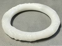 Front view of carved white jade bangle showing surface carvings and smooth finish.
