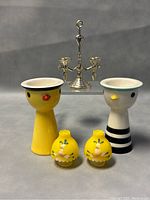 Front view of two egg cup chicks, yellow floral lantern salt and pepper shakers, and silver-tone double candleholder.