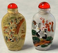 Two vintage Chinese snuff bottles side by side with red stoppers and detailed reversed paintings inside