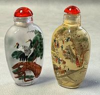 Front view of two small reversed painted glass snuff bottles, one decorated with cranes on pine branches and the other with a detailed Chinese village scene, both with red-orange stoppers.