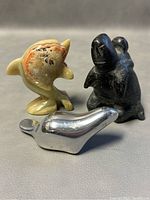 All three figurines displayed on a surface: black Inuit figure, onyx dolphin, and aluminum beaver