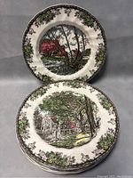 Two Johnson Bros 'The Friendly Village' dinner plates displayed vertically, showing intricate countryside and village illustration.
