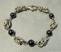 Top view of the silver link and hematite bead bracelet showing its full circular form laid flat on a textured light gray background.
