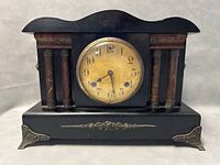 Front view of antique black Waterbury mantle clock showing metal column accents, curved top, and decorative metal feet and base trim.