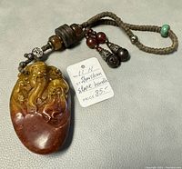 Front view of carved bas relief with beads and bells attached to braided cord