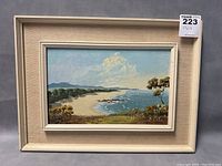 Frontal view of framed oil painting showing coastal landscape, signature at lower right corner and frame wear.