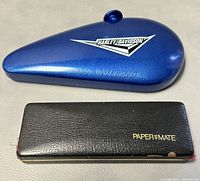 Blue Harley Davidson tank shaped hard case with black Paper Mate pencil case next to it