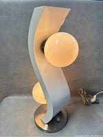 Front angled view showing the lamp's curved white metal body and both globe bulbs, with the brushed metal round base and power cord.