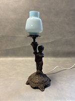 Full view of the old cast metal cherub lamp with blue glass shade, showing the side profile and base details.