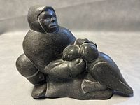 Front angled view of seated Inuit figure holding a bird made from dark gray soapstone.