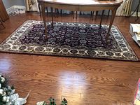 Full view of the burgundy and ivory floral area rug placed on a hardwood floor with a wooden table leg visible.