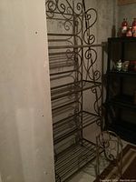Full view of metal bakers rack showing multiple slatted metal shelves and decorative scroll metal sides and back