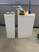 Two white veneer cabinets standing side-by-side with items on top for scale.