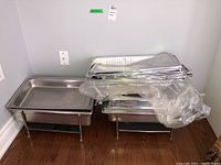 Two stainless steel chafing dishes with legs, some stacked aluminum foil pans in plastic wrapping on top.