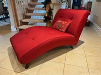 Red chaise lounge seat positioned on a tiled floor showing front and side profile with curved ergonomic shape and tufted upholstery.