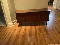 Exterior view of the closed cedar chest showing paneled front and wooden legs on hardwood floor.