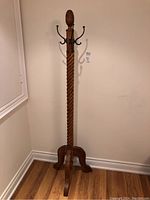 Full height image showing the entire wooden coat rack with twisted post and base standing on a wood floor against a wall.