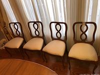 Four wooden dining chairs with upholstered seats arranged side by side, showing the overall design and condition.