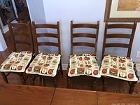 Front view of four wooden ladderback chairs with fruit-themed seat pads arranged against a wall.