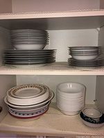Top shelf with stacks of white bowls and plates, some with stripes and floral patterns.
