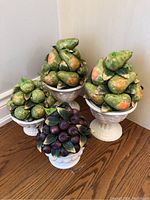 Four faux fruit clusters in white planters, featuring green pears, yellow-green citrus fruits, and purple plums arranged in a group.