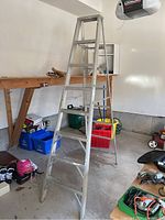 Full view of the aluminum step ladder standing in a garage, showing seven wide front steps and the wide top platform step in a stable A-frame configuration.
