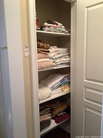 View of shelving unit with neatly stacked folded linens including assorted towels, sheets and blankets in different colors and textures.