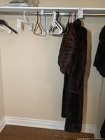 Two dark brown mink fur garments hanging on a rack: full-length coat and matching stole