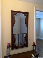 Mirror hanging on wall, showing full vertical view and wooden framed decorative edges.