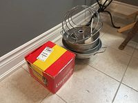 Image with the pasta maker box and stacked kitchen items including baking pan, bundt mold, and strainer on tile floor.
