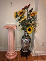 Full view of ceramic pillar plant stand beside Asian vase with faux sunflower arrangement.