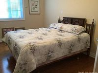 Queen size wooden bed frame with ornately carved headboard, mattress, and floral comforter and pillows set in bedroom.