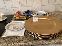 Golden charger plates stacked beside a rooster platter and other decorative plates on countertop