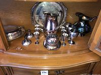 Full set of silverplate items arranged inside a wooden cabinet, including trays, pitchers, goblets, cups, and covered dish.